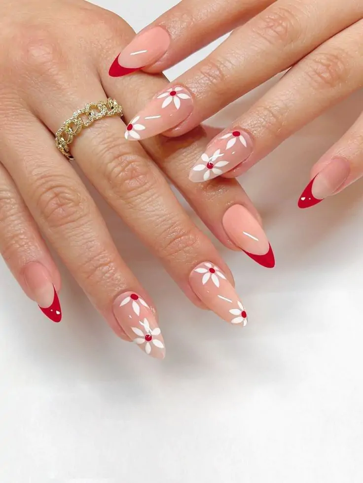 This set features a soft nude base that enhances the natural beauty of the nails while keeping the design fresh and minimal. The red French tips with a curved, almond shape add a bold yet elegant touch. Delicate white daisy flowers with red gem centers bring a playful and feminine vibe, making the design perfect for a chic and stylish look. Thin white accent lines add depth and detail, balancing the floral elements with a modern touch. The glossy finish enhances the vibrancy of the red and white details, making the nails look polished and refined.