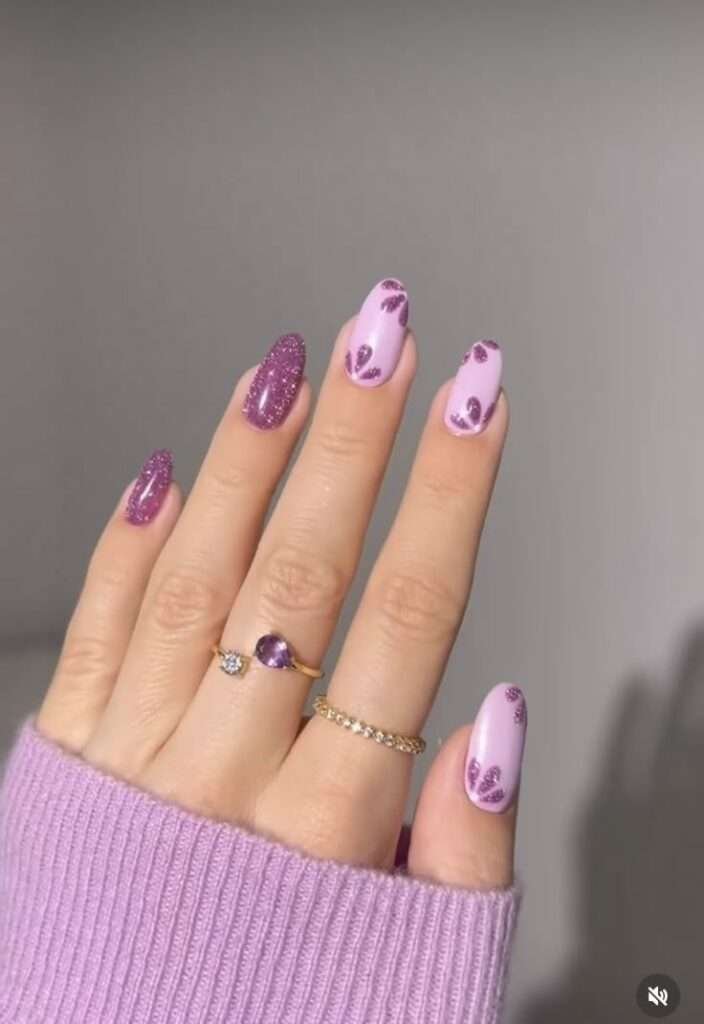 This manicure features a soft pastel lavender base, creating a feminine and elegant look perfect for spring. The glittery purple accent nails add a touch of glamour, making the design stand out with a luxurious feel. Subtle glitter heart details on the pastel nails enhance the romantic and playful vibe. The almond shape complements the delicate color palette, elongating the fingers for a chic and refined appearance. A high-shine top coat ensures a flawless finish, adding durability and a salon-quality glow.