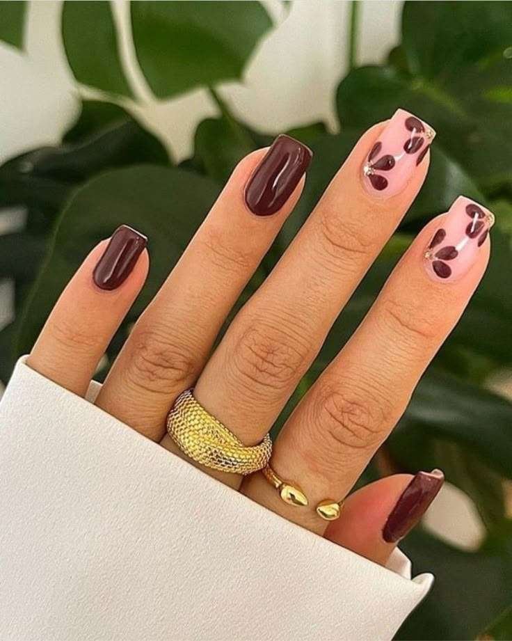 This manicure features rich chocolate polish for a dramatic appearance. The pale pink base with abstract brown hearts provides an artistic element. A glossy finish brings out the depth and contrast of the dark color. The square nail shape gives it an elegant look, ideal for a classy environment. Delicate gold accents give the design a luxurious feel.