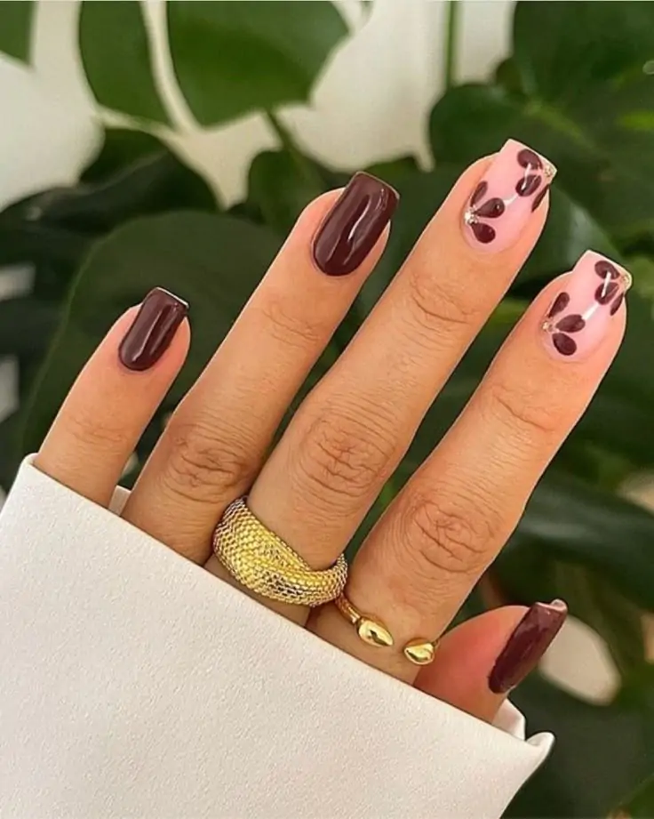 This manicure features rich chocolate polish for a dramatic appearance. The pale pink base with abstract brown hearts provides an artistic element. A glossy finish brings out the depth and contrast of the dark color. The square nail shape gives it an elegant look, ideal for a classy environment. Delicate gold accents give the design a luxurious feel.