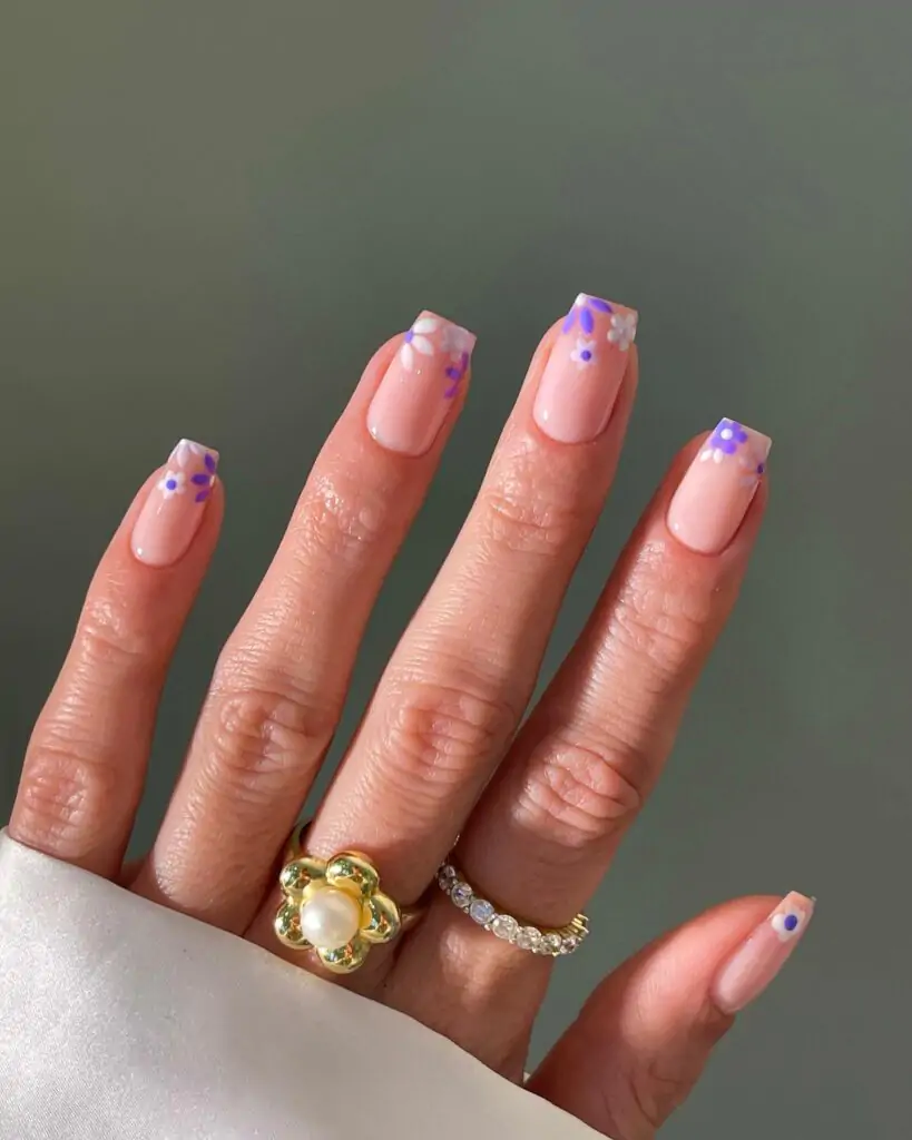 Floral tips nails is a fashionable nail art wherein tips are adorned with dainty flower patterns. They usually have a pale pink background and bright purple and yellow patterns at the tips. It's a playful way of adding a touch of nature to your look!