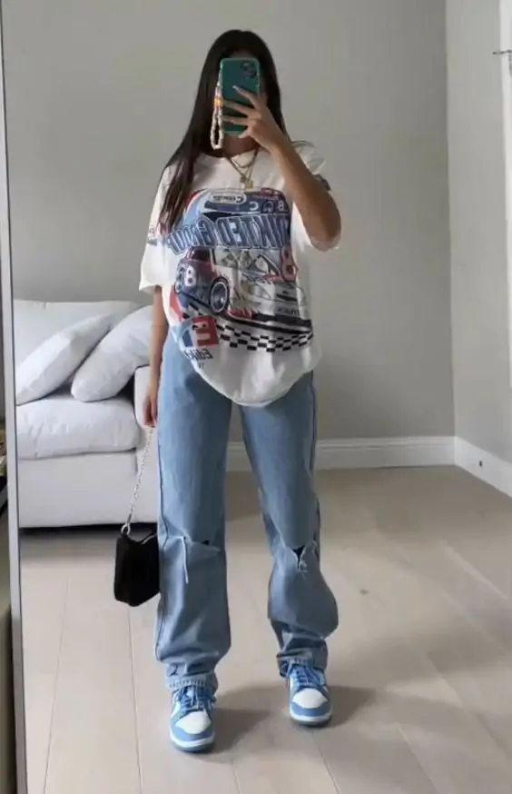 This outfit showcases an oversized graphic tee paired with distressed blue jeans and matching blue sneakers. It’s a trendy, laid-back look ideal for casual outings