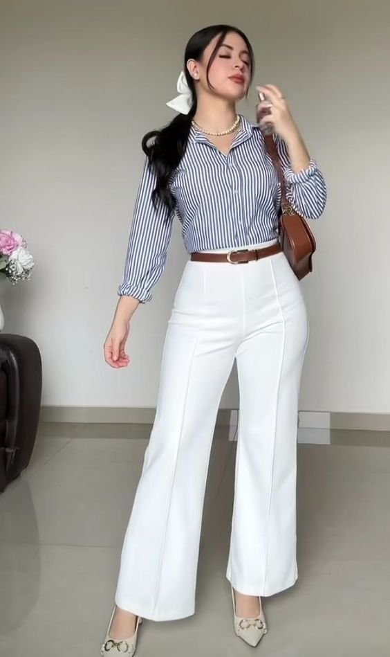 Woman wearing a navy striped blouse with high-waisted white pants, a brown belt, and accessorizing with a pearl necklace and a white bow in her hair.