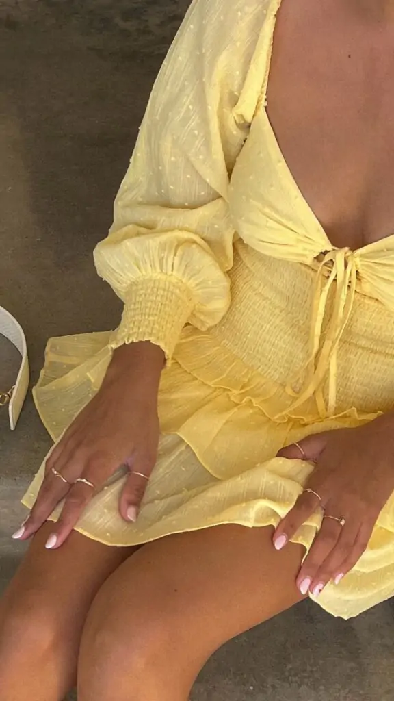 Person in chic yellow summer dress with puffed sleeves and white high heels seated on steps.