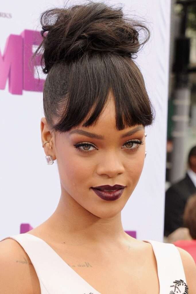 Rihanna's modern-day Cinderella style is a tale of two textures: sleek bangs offset a chic, chunky bun. Rihanna messy bun, bold messy bun, edgy hairstyle, celebrity hairstyle, Rihanna hair