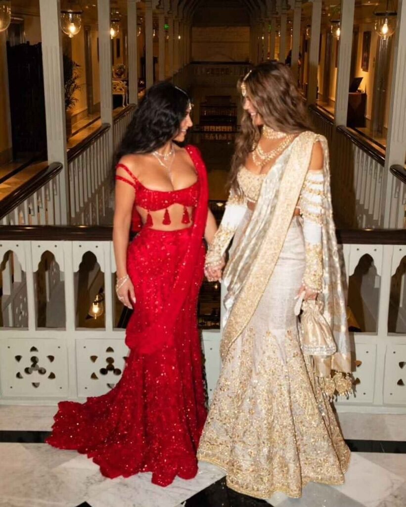 Kim Kardashian and Khloe Kardashian holding hands, wearing beautiful traditional Indian outfits at the Ambani wedding.