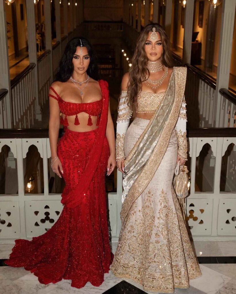 Kim Kardashian and Khloe Kardashian holding hands, wearing beautiful traditional Indian outfits at the Ambani wedding.