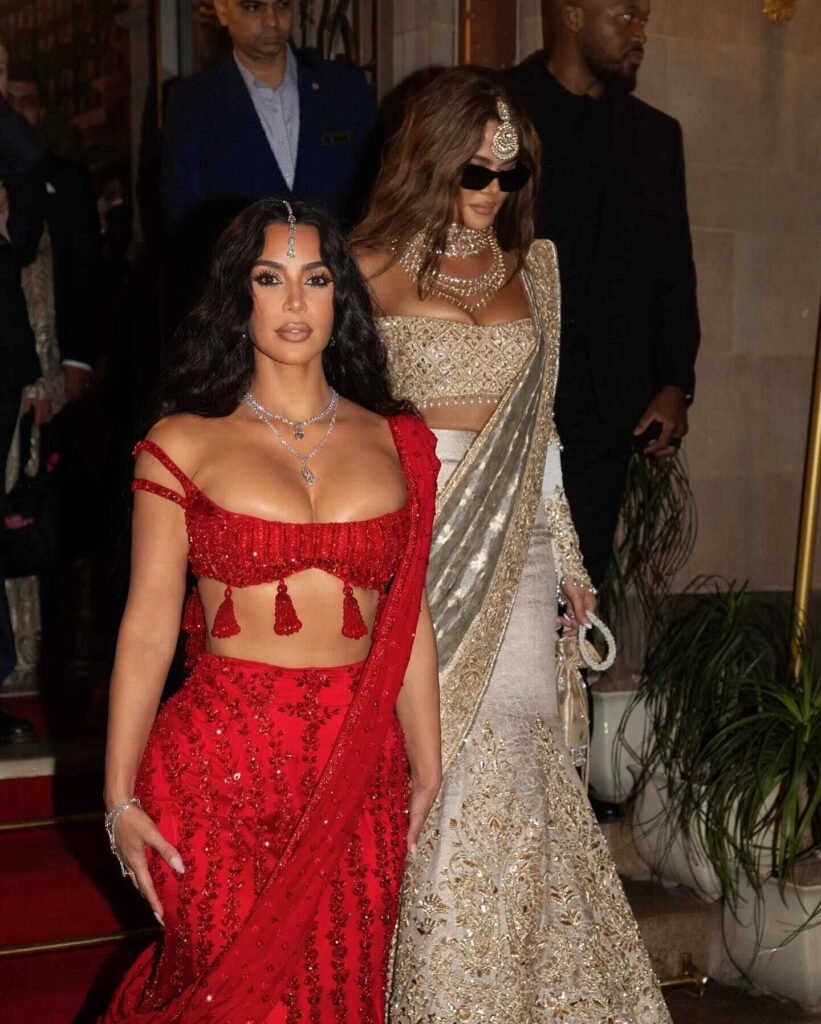 Kim Kardashian and Khloe Kardashian holding hands, wearing beautiful traditional Indian outfits at the Ambani wedding.