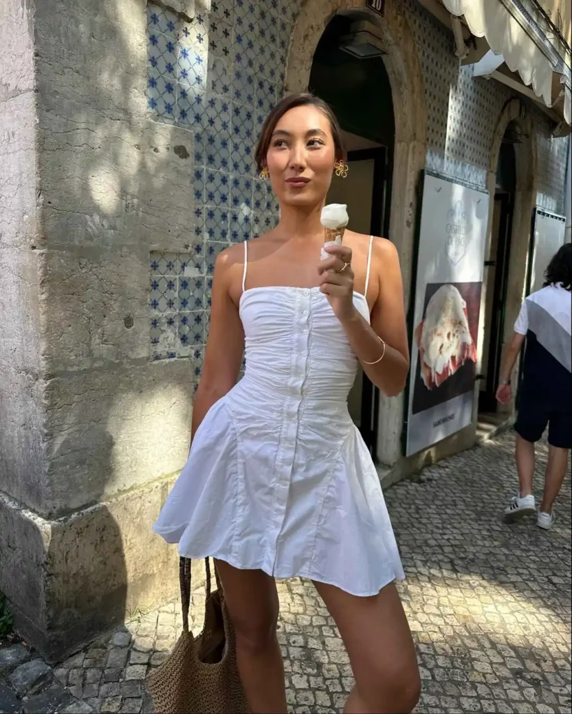 Fashionable summer street style featuring white strapless mini dress with ruched detail and woven tote bag.