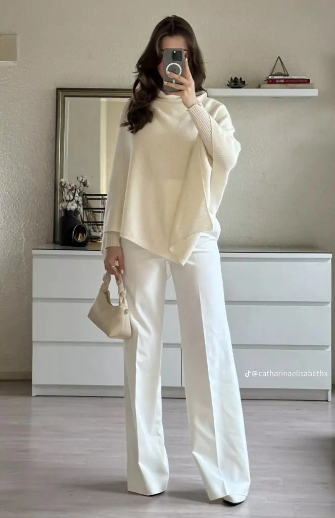 Woman wearing a white oversized sweater with wide-leg trousers and a small handbag.