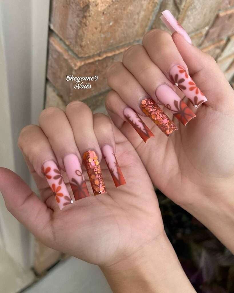 Fall nail art featuring warm orange and pink hues with intricate leaf patterns and sparkling accents