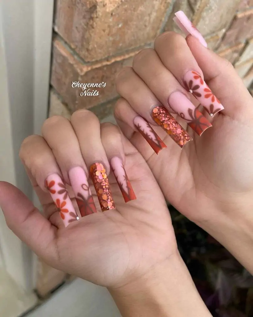 Fall nail art featuring warm orange and pink hues with intricate leaf patterns and sparkling accents