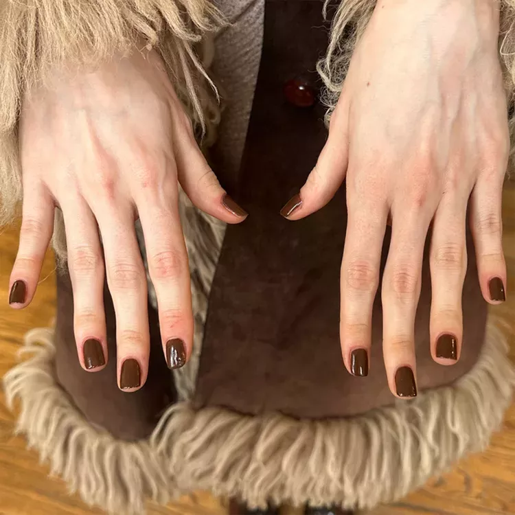 Hands displaying glossy deep brown nail polish suitable for fall fashion