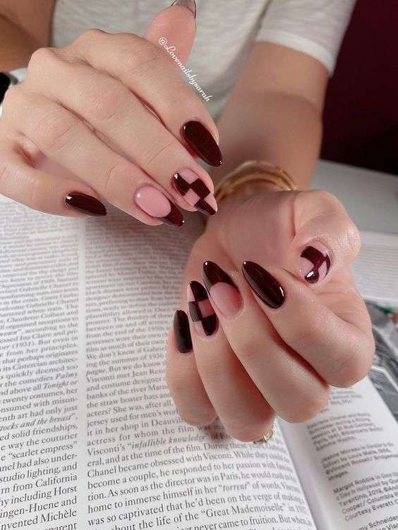 Hand with deep burgundy nails and a nude accent nail with black geometric pattern, perfect for autumn.