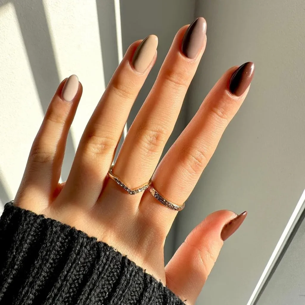 Hand displaying almond-shaped nails with gradient colors from beige to brown for fall.