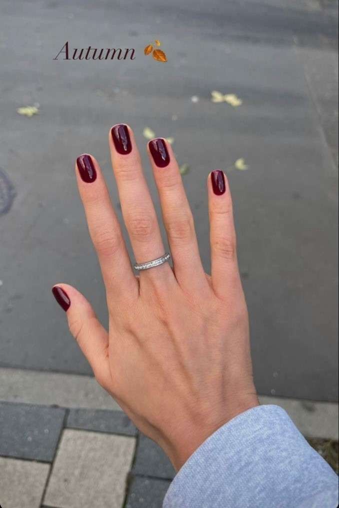 Hand with deep burgundy nail polish and a silver ring, showcasing elegant fall nail art.