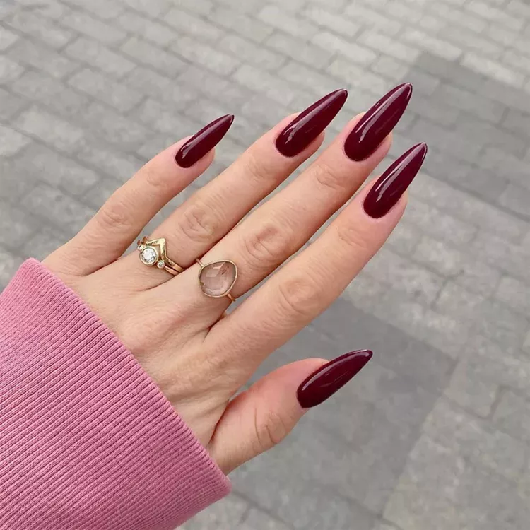 Deep burgundy long pointed nails with gold rings.