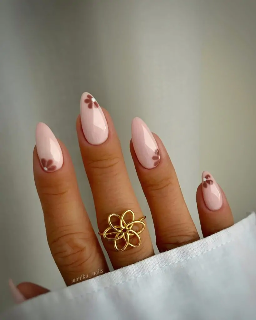 Hand displaying fall-inspired almond-shaped nails in nude pink with subtle brown leaf designs.