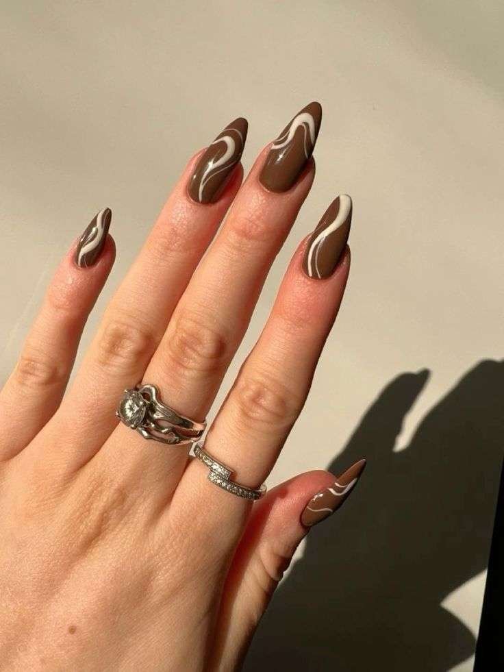  Hand with long, almond-shaped nails painted in fall colors with a glossy finish and accessorized with rings.