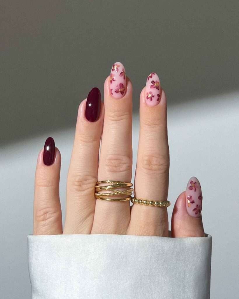 Fall nail design with rich burgundy hues, delicate floral accents on a nude base, and almond-shaped nails