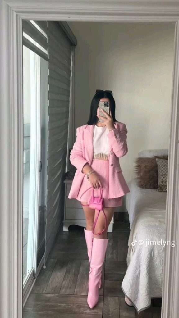 Fashion-forward individual in monochromatic pink power suit with matching thigh-high boots and handbag posing for a mirror selfie.