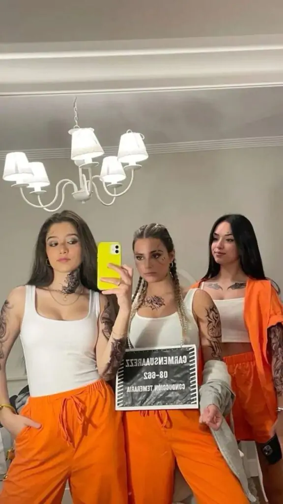 Three people posing for a selfie in prison-inspired Halloween costumes with bright orange pants and white tops.