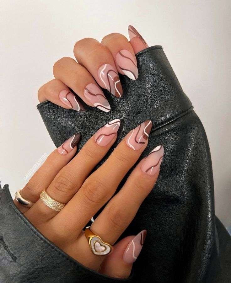 Hand with almond-shaped nails featuring a marbled pattern in beige and brown, perfect for autumn..