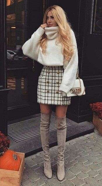 Woman wearing a white turtleneck sweater, plaid mini skirt, taupe over-the-knee boots, and a designer shoulder bag.