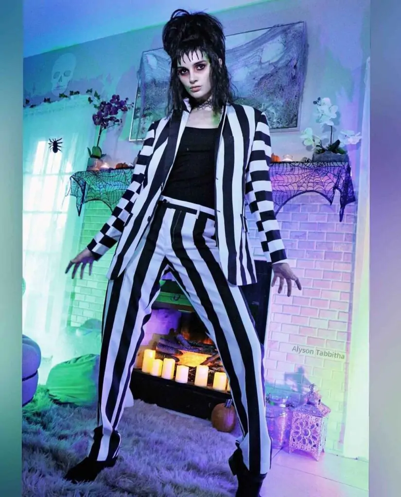 Your outfit is a black and white striped suit with a black top, inspired by Beetlejuice. Let’s call it “The Ghost with the Most.” This costume is a nod to Tim Burton’s 1988 film, “Beetlejuice,” loved for its quirky and spooky vibes. People adore it for its unique look and nostalgic charm.