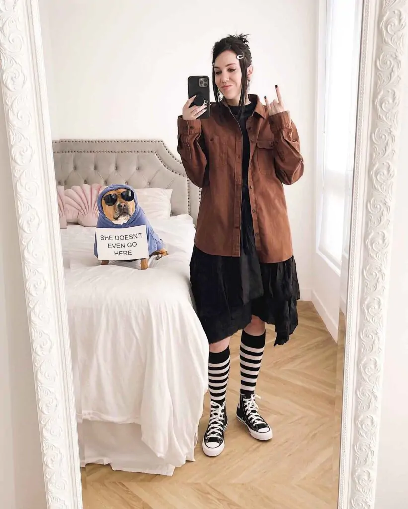 Retro Rebel Halloween costume. The outfit features a brown jacket over a black dress, paired with black-and-white striped knee-high socks and black Converse sneakers. I’d call it "Retro Rebel."