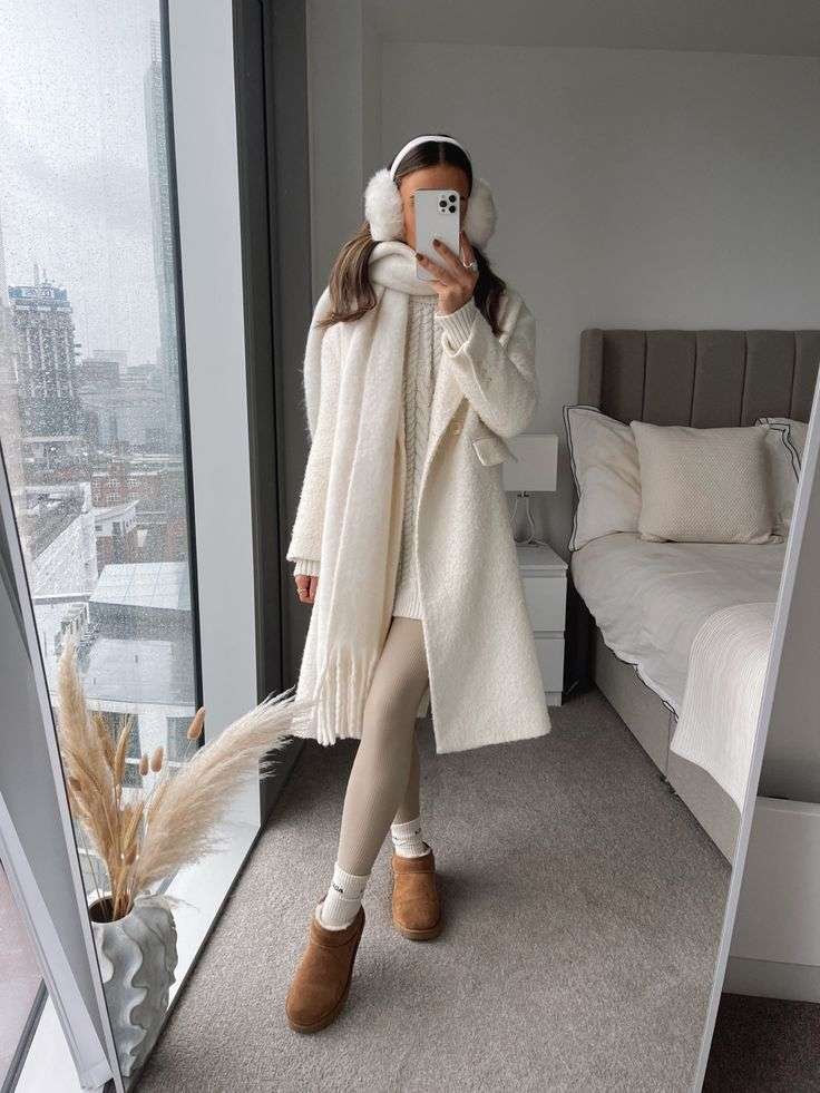 A long white coat paired with a matching scarf is perfect for winter. Beige leggings and brown ankle boots complete the cozy look. Accessories include white earmuffs and a headband to keep you warm.