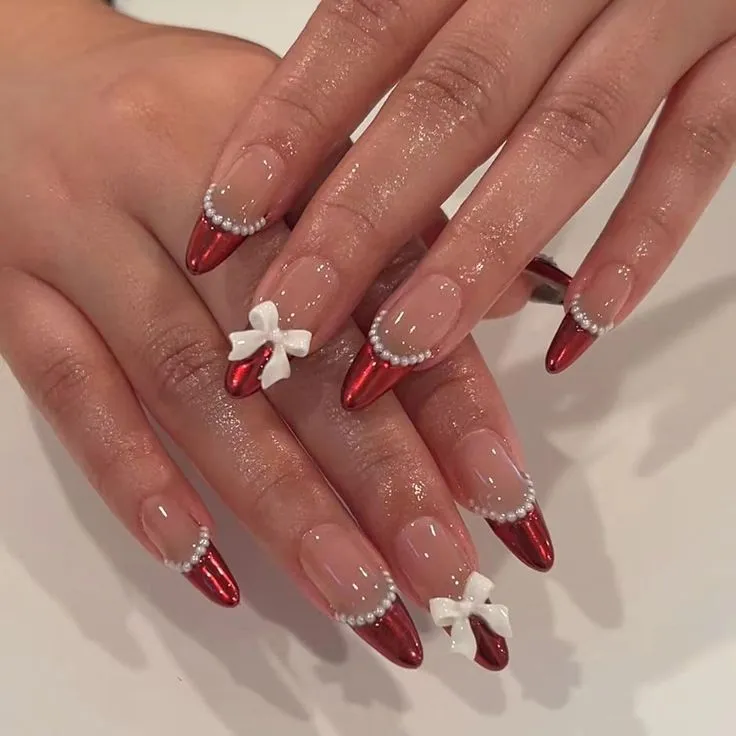 These winter nails feature elegant red metallic tips adorned with white pearls. Two nails on each hand boast a white 3D bow, adding charm and sophistication. Perfect for holiday celebrations, this festive design is called "Winter Elegance."