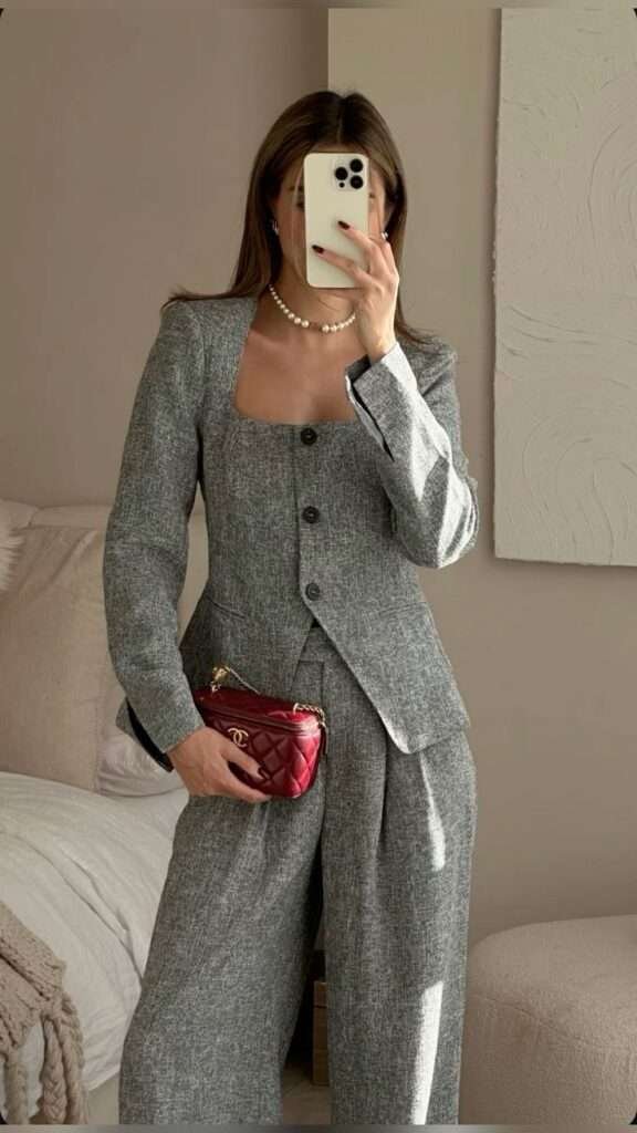 This chic winter outfit features a tailored grey pantsuit with a square-neck blazer and matching high-waist trousers, perfect for an elegant and polished look. The red Chanel quilted mini bag adds a pop of color, while the classic pearl necklace complements the sophisticated vibe. Ideal for work or formal events, this ensemble balances style and professionalism effortlessly.