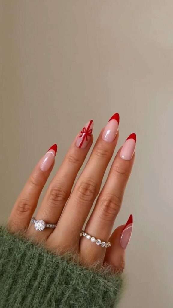 The nails have a sheer, natural base, creating a clean and understated backdrop. The tips are accented with a classic red French manicure, providing a pop of holiday color. On one or two accent nails, delicate red lines form the shape of a ribbon and bow, as if a tiny present has been tied directly onto the nail. This design is charming and whimsical, capturing the spirit of giving and the joy of the holiday season in a subtle and sophisticated way.