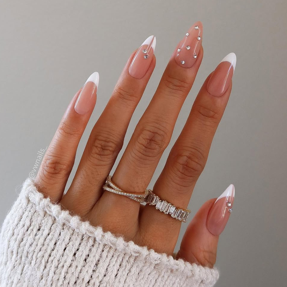 Delicate rhinestones are strategically placed on some nails, mimicking the glistening effect of ice crystals. This elegant manicure features a sharp stiletto nail shape with a classic white French tip for a clean and sophisticated look. The combination of the sharp shape, clean white tips, and subtle sparkle creates a chic and frosty winter aesthetic.