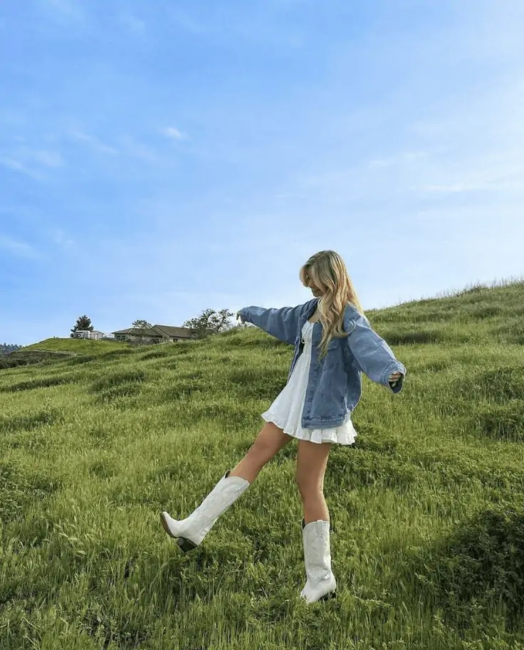 Imagine a sunny day on a grassy hill, where you exude spring vibes in a stylish white dress paired with a classic blue denim jacket. Add white cowboy boots for a dash of western charm. This outfit is perfect for a day of carefree fun in the great outdoors.