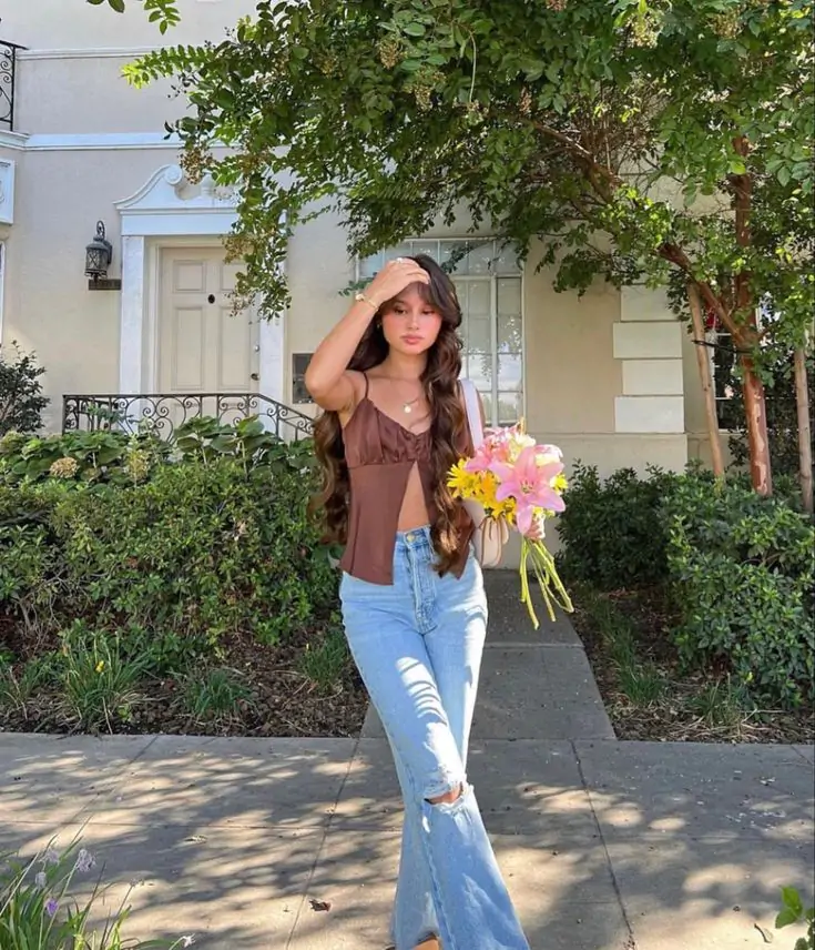 Imagine walking through the charming streets of your city on a sunny spring day. You’re wearing a stylish brown top paired perfectly with light blue jeans, exuding casual elegance. With a bouquet of fresh flowers in one hand, you’re ready to embrace the season’s beauty. The greenery and sunlight around you add the perfect backdrop to this refreshing look.