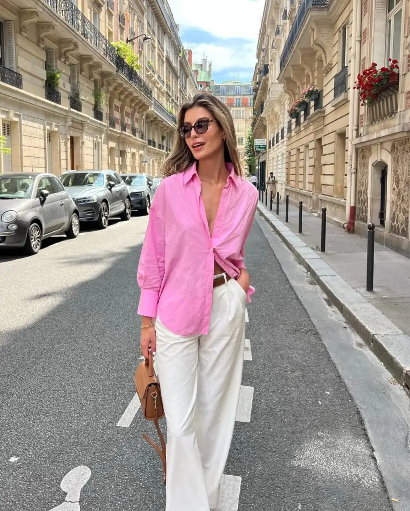 "Picture yourself strolling through historic European streets, soaking in the charm of timeless architecture." You’re dressed in a stylish pink shirt and crisp white pants, effortlessly blending elegance with a modern touch. A brown handbag adds a refined sophistication to the look. This outfit is perfect for exploring a city adorned with vibrant balconies and blooming flowers, capturing the essence of a chic, European getaway.