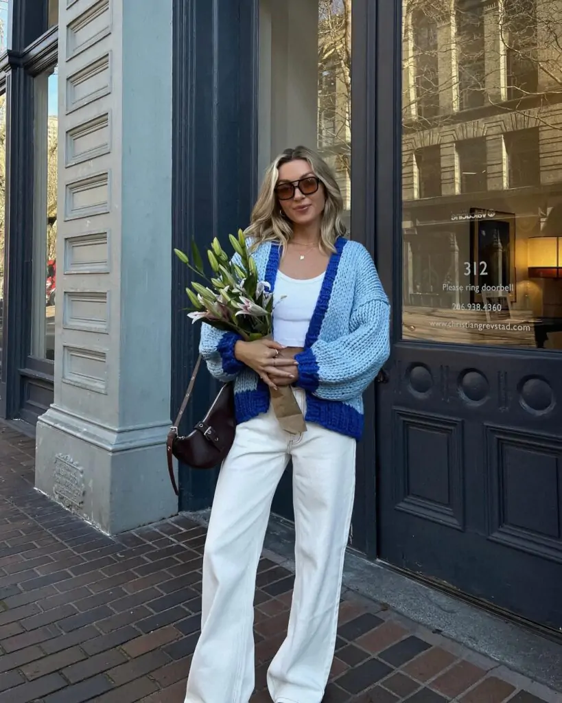 Feel the beauty of spring with a look that’s both cozy and chic. A light blue and dark blue cardigan adds a warm, layered touch over a crisp white top and white pants, creating a perfect blend of comfort and style. Paired with a brown shoulder bag and a fresh bouquet of flowers, this outfit is ideal for a day of exploring the city, capturing the essence of effortless spring charm.