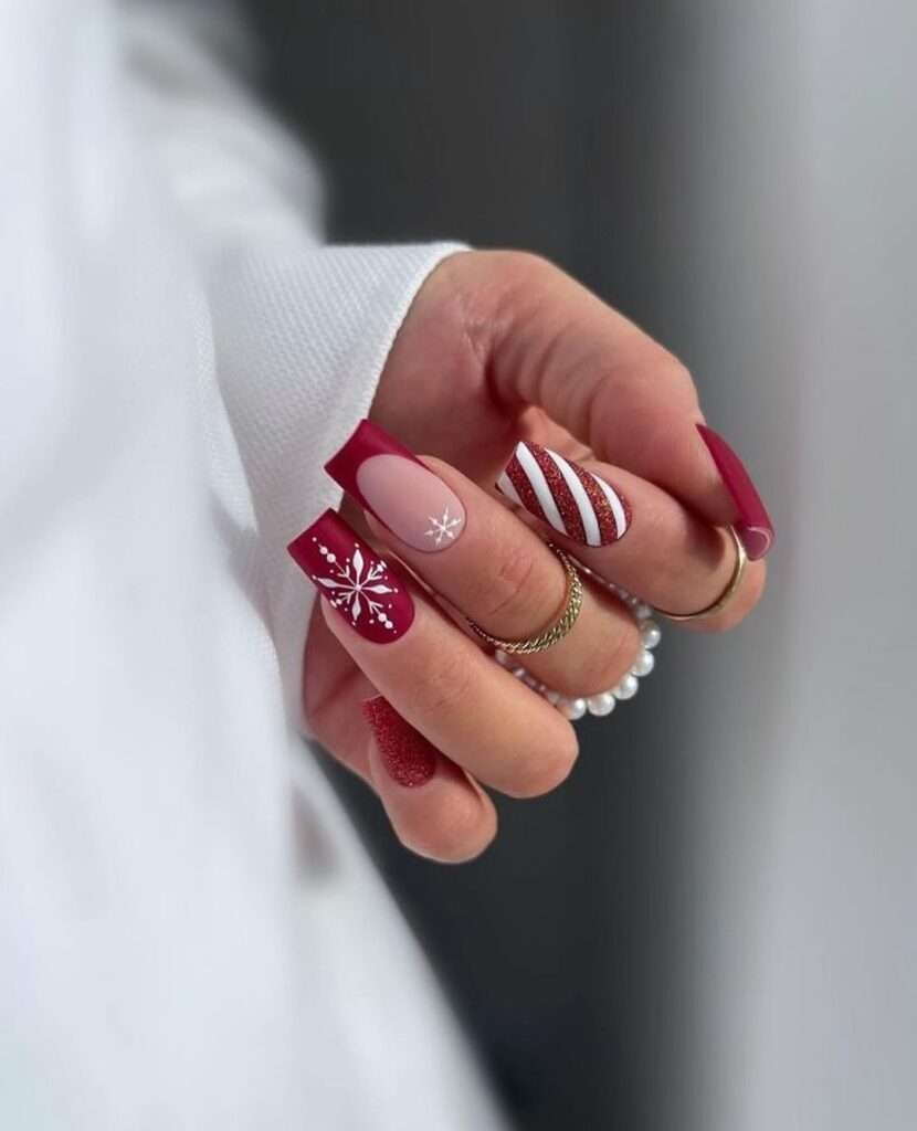 Delicate white snowflakes adorn some nails, evoking the gentle beauty of a winter snowfall. This festive manicure uses a deep crimson red as its dominant color, creating a rich and luxurious backdrop. Candy cane stripes on an accent nail add a playful touch, completing this elegant and festive holiday design.