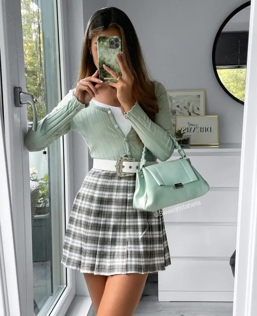 Step into spring with style." A light green cardigan over a white top and plaid pleated skirt creates a fresh, coordinated look. Add a white belt and matching light green handbag for the perfect finishing touch. Ideal for a day out enjoying the season.