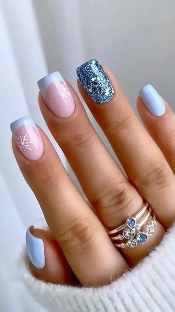 These festive nails feature a soft pink and blue base with a French tip accented with silver glitter and snowflake designs. The combination of cool tones and wintery motifs creates a sophisticated and elegant look, perfect for the holiday season.