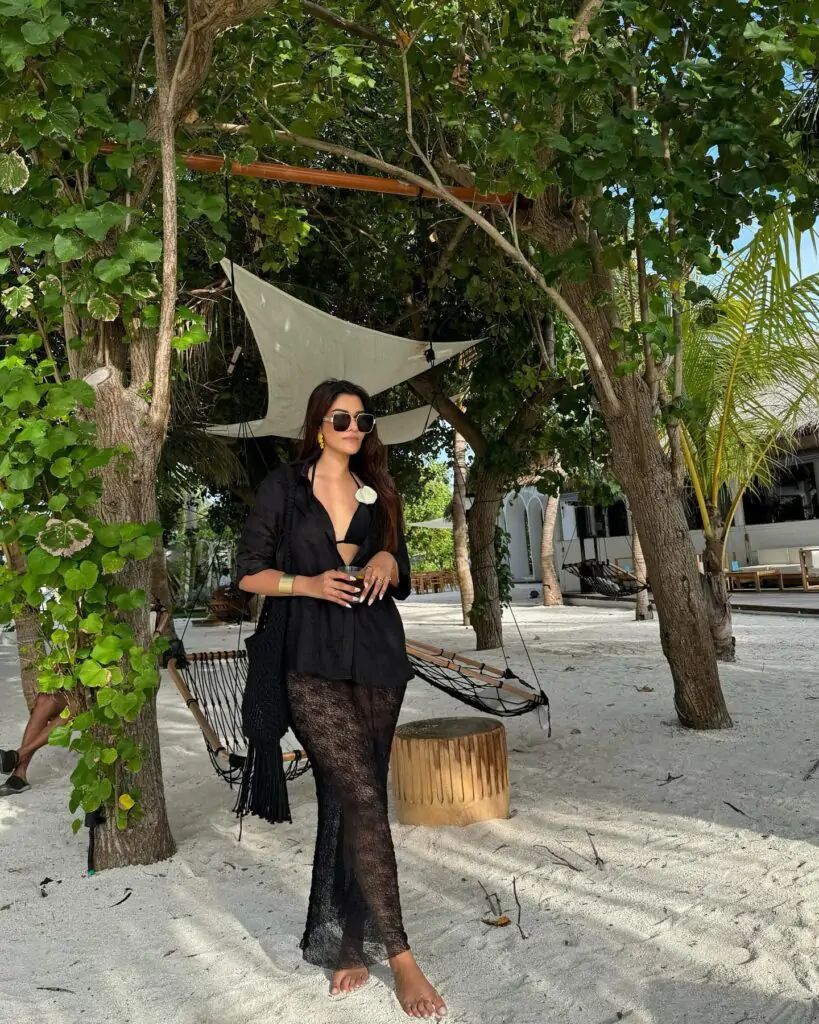 Oversized black sunglasses with a chic, minimal design, adding a stylish touch to the beach outfit. A sheer lace skirt, replacing jeans, adds an elegant and flowy beach vibe. An oversized black button-up shirt worn open for a casual yet sophisticated look.