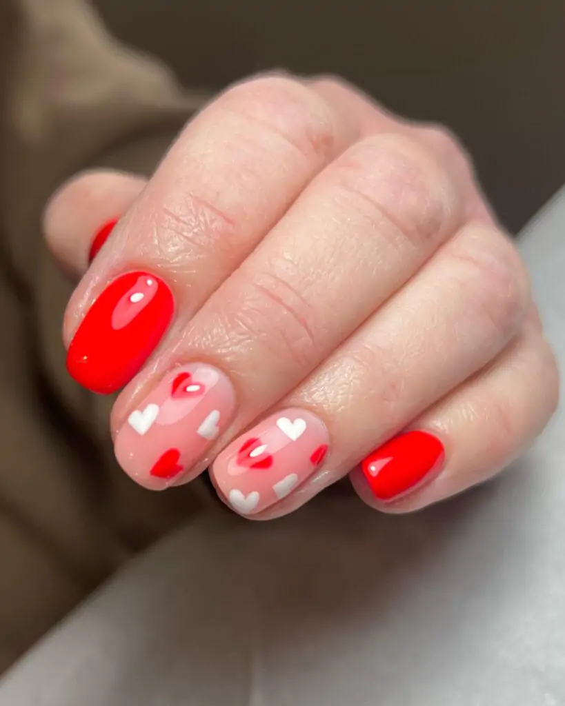 Fall in love with this playful Valentine's Day manicure! A mix of classic red and soft pink nails are adorned with scattered white hearts, creating a sweet and romantic look. It's a design that's perfect for spreading the love all season long.