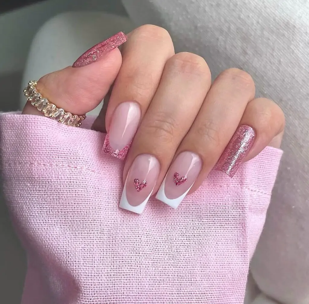 This manicure is a dreamy blend of classic and trendy! Soft pink nails are accented with a delicate white French tip and a touch of shimmering glitter. The standout feature is the adorable tiny hearts peeking from under the French tip, adding a touch of playfulness.