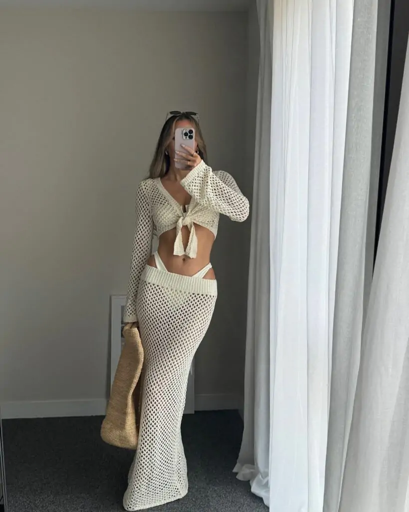 A mesmerizing crochet ensemble featuring a long-sleeve top with a chic front tie and a high-waisted skirt with stylish cut-out sides, perfectly revealing your beach-ready bikini. Complete the look with a large woven straw bag for that ultimate boho-chic flair.