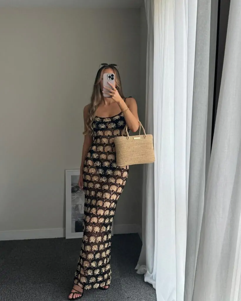 Effortlessly chic, this beach-ready look features a black maxi dress adorned with vibrant floral patterns, paired with a woven straw tote and sleek sandals, perfect for a stylish seaside escape.