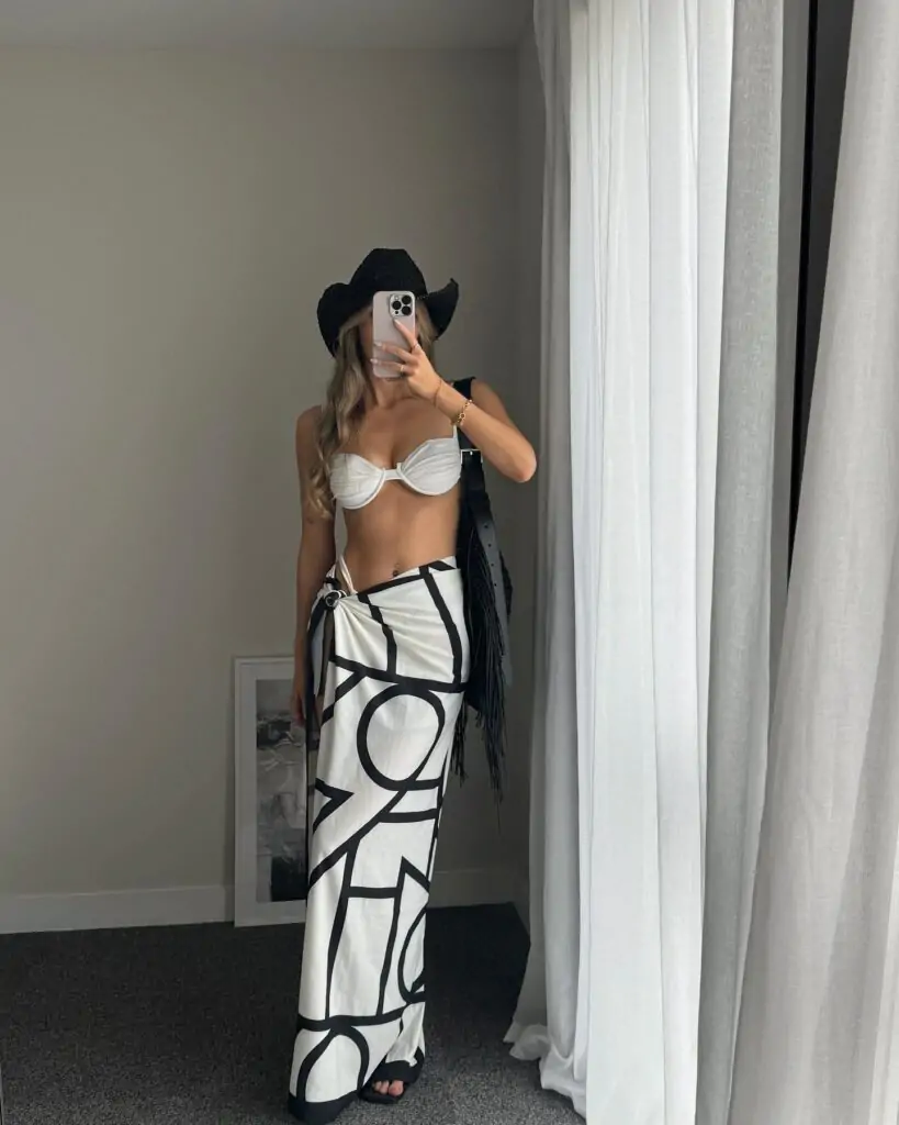 Elevate your beach look with a white bikini, statement graphic sarong, and black cowboy hat for a bold, boho-inspired coastal vibe.