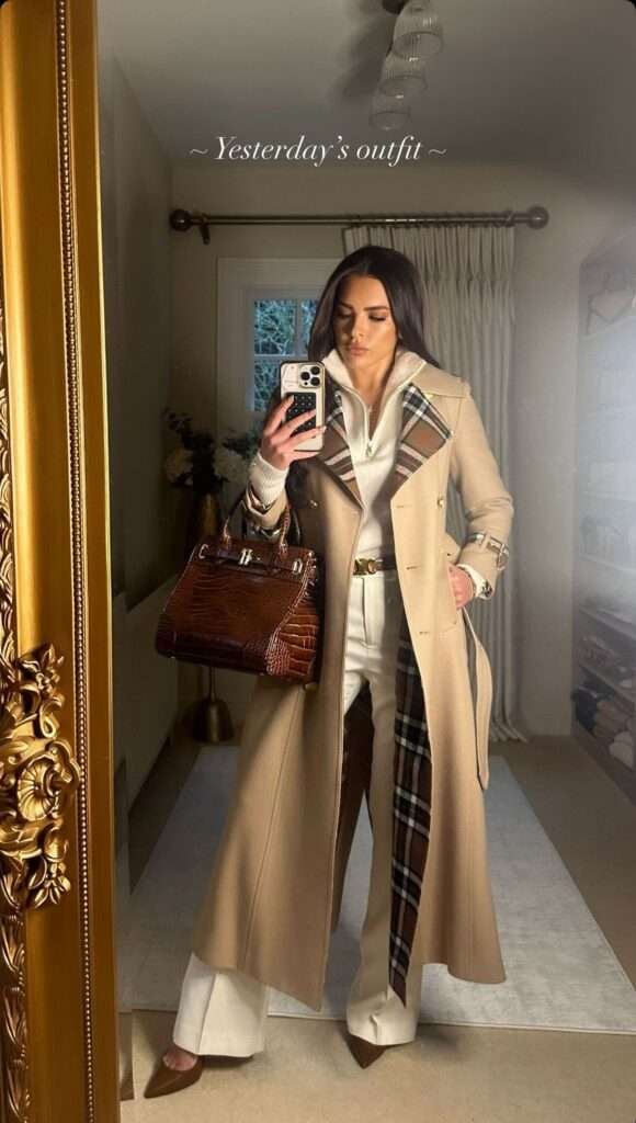 The Trench Reimagined: A classic camel coat is instantly elevated with a dramatic maxi length and striking plaid lining, offering a flash of heritage pattern with every step. Master the High-Low: Layer the outerwear over crisp, high-waisted wide-leg white trousers and a sporty half-zip knit, perfectly blending tailored luxury with cozy athleticism. Finish with Richness: Accessorize with a deep brown, crocodile-embossed structured bag and matching pointed heels, creating a polished, autumnal power statement.