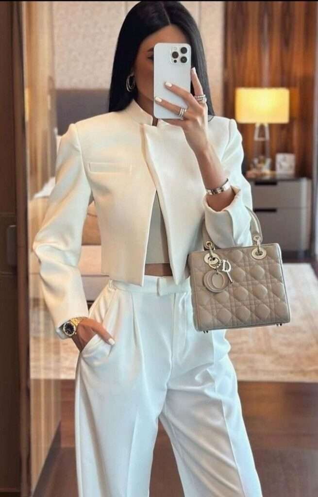 Elevate your workwear with the sharp minimalism of a monochromatic ivory ensemble, featuring a chic, collarless cropped blazer for a modern, architectural silhouette. Detailing is everything: the high-waisted, pleated wide-leg trousers create a beautiful flow, subtly showing a hint of midriff for contemporary sophistication. Finished with quiet luxury via a quilted, nude Dior Lady bag and layered silver jewelry, this look defines refined, boardroom-ready glamour.